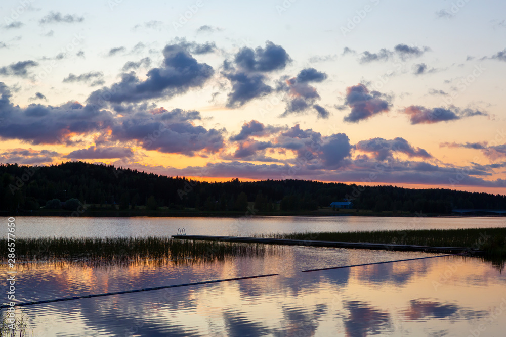 Fototapeta premium Sunset at the lakeside in Finland during summer evening. Glowing orange horizon.