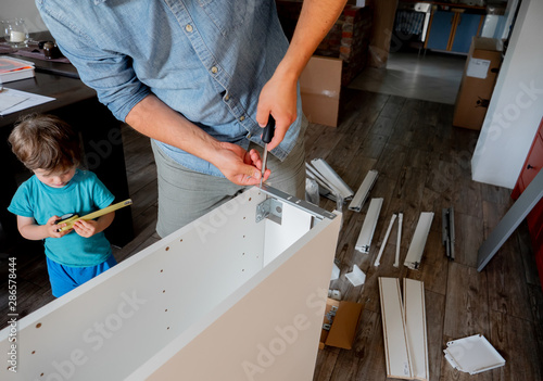 Young man with screwdriver and a child are instaling a furniture