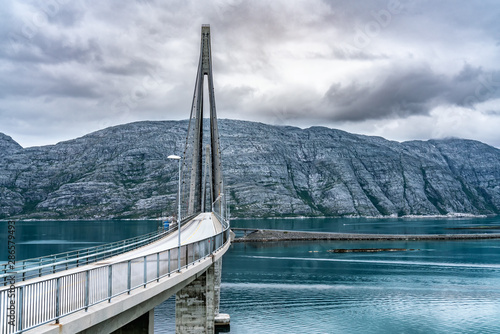 Dramatic photo of Helgelandsbrua (norwegian) or Helgeland Bridge is Norway's finest bridges between Alstahaug and Leirfjord at Helgeland, Norway. At Sandnessjoen town. Cloudy and quiet summer weather photo
