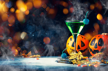 Halloween composition with festive drink, green cocktail and pumpkins lanterns, smoke and fallen leaves on night dark blue background, selective focus