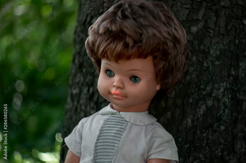 A female doll in white clothes is standing near a tree trunk. A female doll in white clothes is standing near a tree trunk.