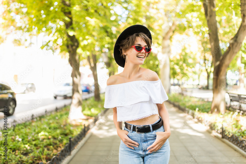 Beautiful young woman in hat and sunglasses walking in the city. Beautiful young woman in hat and sunglasses walking in the city.