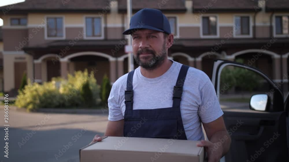 Close-up of pizza deliveryman walking along houses holding boxes, sunlight illuminating roofs. Adult worker of food delivery service carrying order to client delivering pizza at home Close-up of pizza deliveryman walking along houses holding boxes, sunlight illuminating roofs. Adult worker of food delivery service carrying order to client delivering pizza at home
