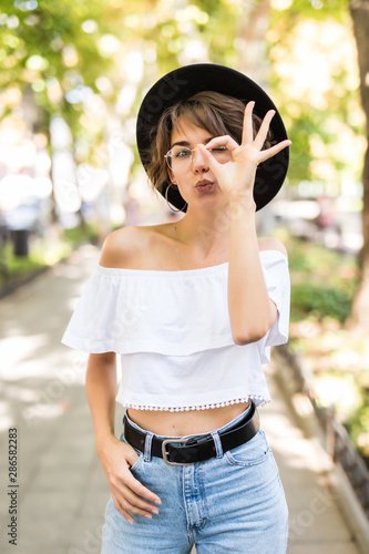 Young girl with pink shirt showing an ok sign with fingers at city