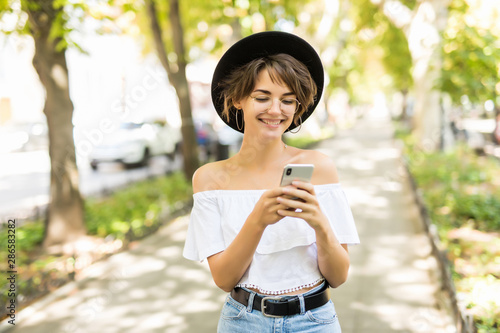 Happy young woman wearing in hat reading good news from her mobile phone. Urban scene.