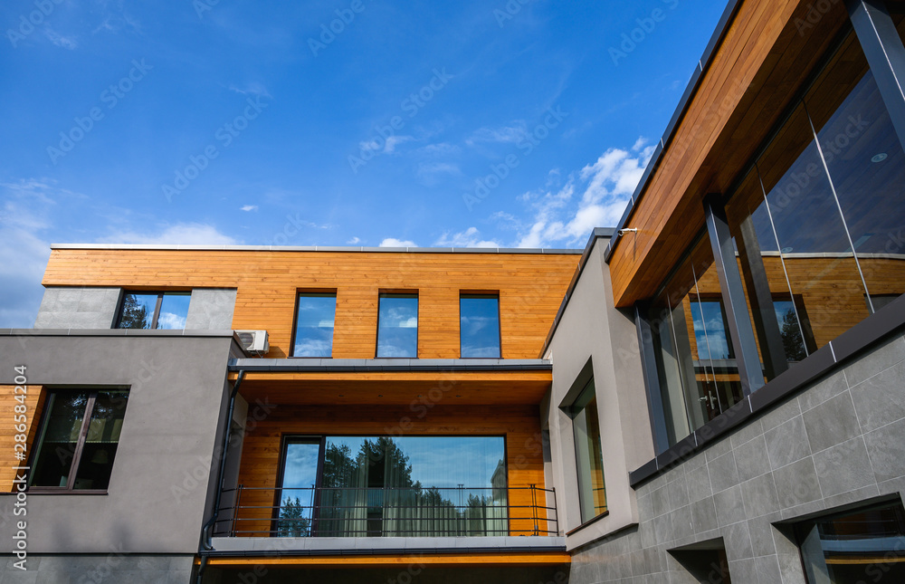 Modern new house exterior, facade with natural wood and many windows on blue sky background