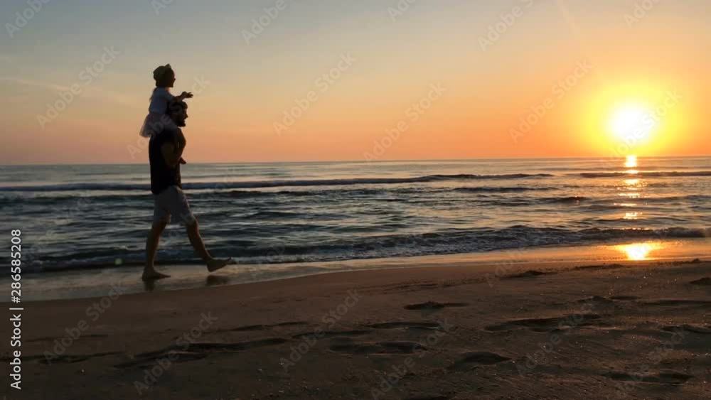 Father and daughter walking along the beach at sunset. Father and daughter walking along the beach at sunset.