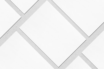 Closeup of empty white rectangle poster mockups lying diagonally with soft shadow on neutral light grey concrete background. Flat lay, top view. Open composition.