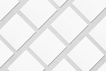 White empty square business card mockups with soft shadows lying diagonally on neutral light grey concrete background. Flat lay, top view. Open composition.