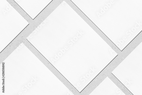 Closeup of empty white rectangle poster mockups lying diagonally with soft shadow on neutral light grey concrete background. Flat lay, top view. Open composition. photo