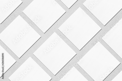 White empty square business card mockups with soft shadows lying diagonally on neutral light grey concrete background. Flat lay, top view. Open composition.