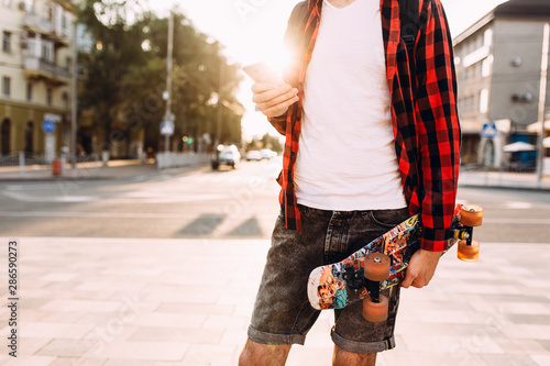 guy with a beard, walks around the city with a skateboard and a smartphone in his hands