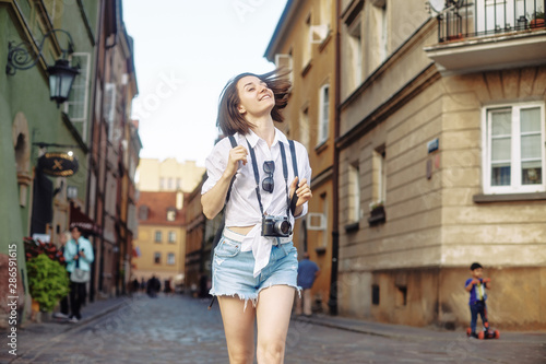 The girl in the black hat and sun glasses with photo camera on a road in an old european town. © Sotnikow