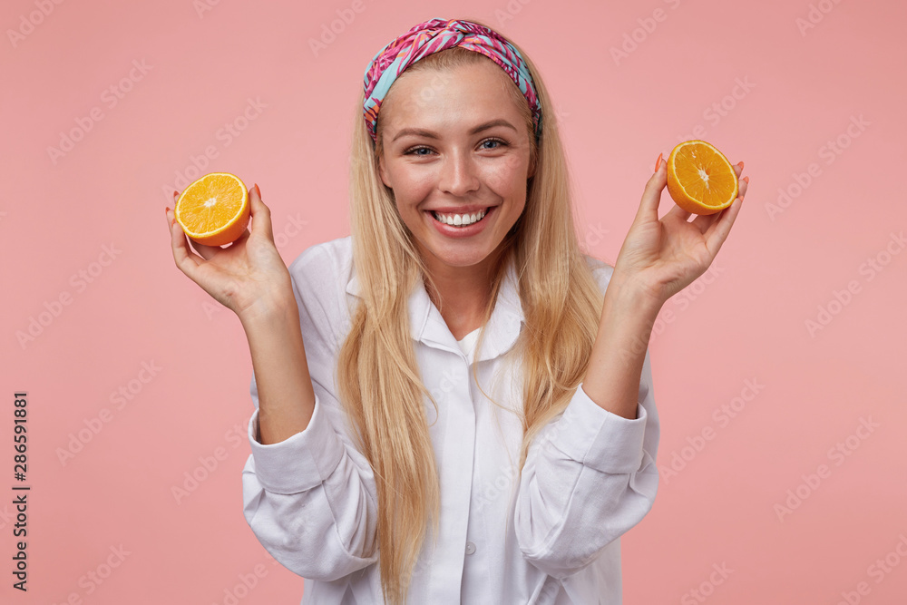 Portrait of lovely cheerful young woman with halves of orange in her hands, looking to camera with wide smile, isolated over pink background Portrait of lovely cheerful young woman with halves of orange in her hands, looking to camera with wide smile, isolated over pink background