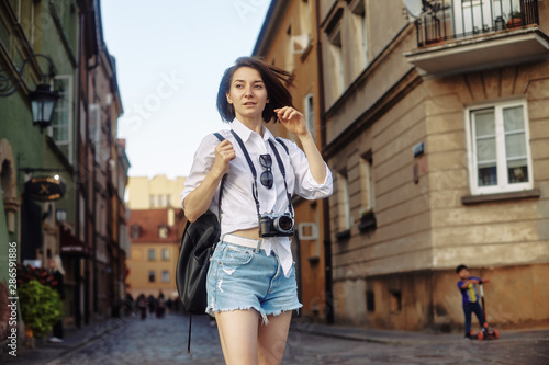 The girl in the black hat and sun glasses with photo camera on a road in an old european town. © Sotnikow