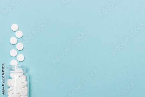 Big white medicine tablets in transparent glass bottle on light blue background with copy space for your text. Template medical blog social media. Flu season concept. health care concept.