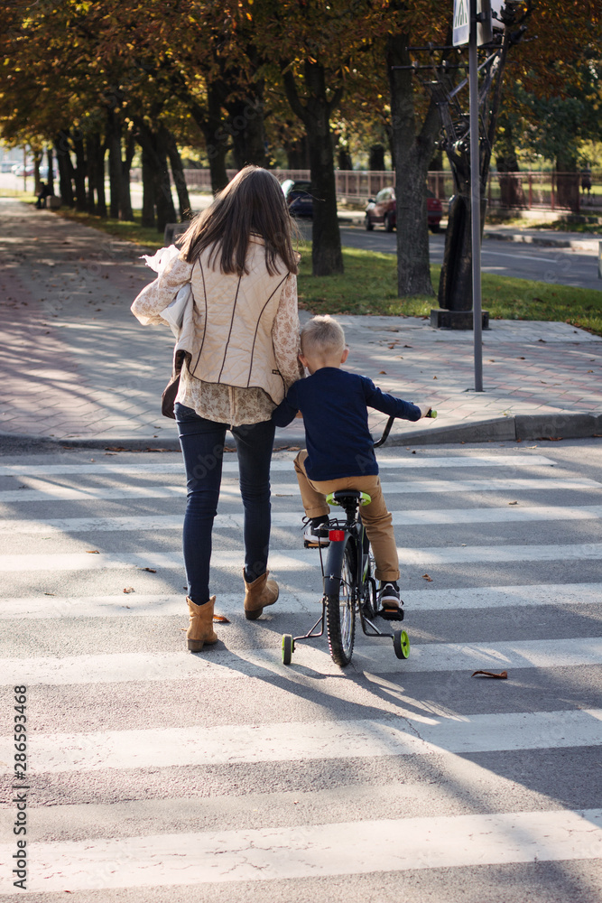 Mom is helping the son on bicycle to cross the road at a pedestrian crossing