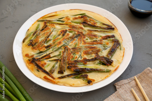 Homemade korean Pajeon scallion pancake on a white plate on a gray background, side view. Asian food. Close-up.