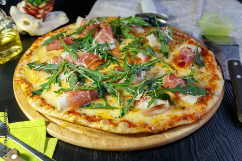 Pizza with bacon, cheese and herbs on a wooden dish on a black wooden background