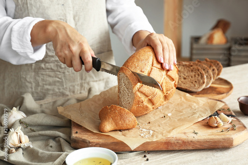 Woman cutting fresh bread in kitchen, closeup