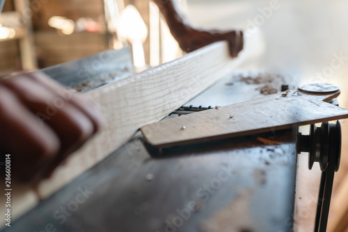 Woodworking machine process a wooden plank. Workers hands hold a wooden plank. Selective focus. Motion blur. Manual wood processing concept.