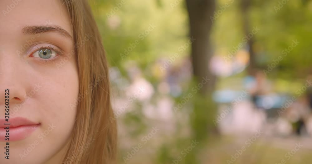 Closeup half face portrait of young cute caucasian female looking at camera smiling happily standing in park outdoors Closeup half face portrait of young cute caucasian female looking at camera smiling happily standing in park outdoors