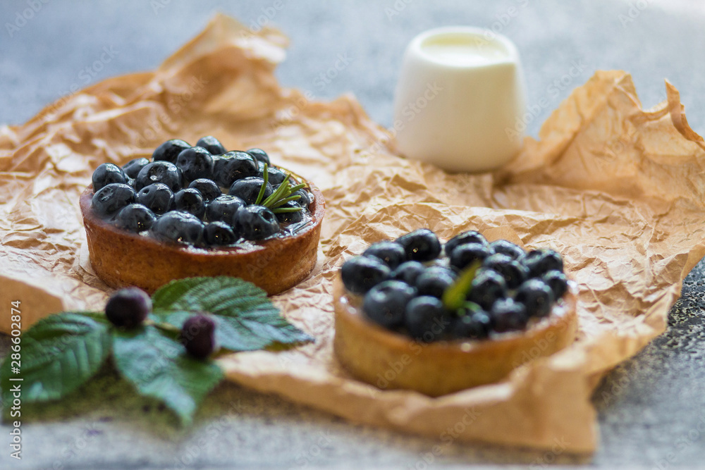 Tartalets with fresh berries on rumpled paper on a grey surface. Tartalets with fresh berries on rumpled paper on a grey surface.
