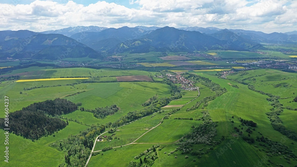 Aerial view of fields, meadows and hills under High Tatras mountains, some settlements and roads also visible. Photograph taken during cloudy summer season.  