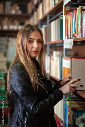 Beautiful teenager schoolgirl choosing a book in the library