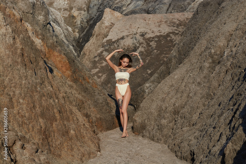 Asian girl with a tattoo stands in the mountains in a white bikini