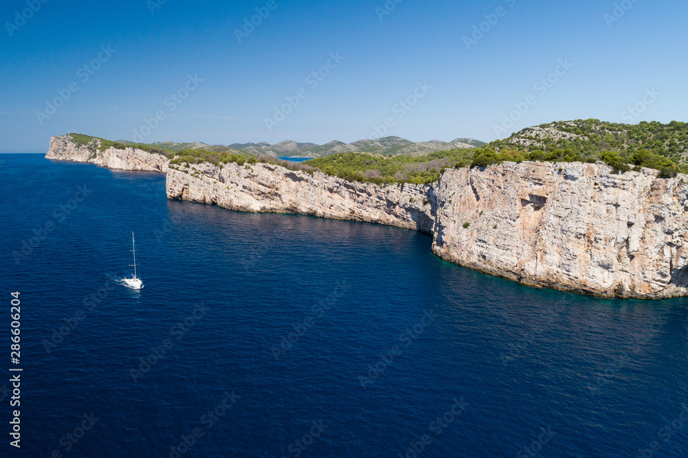 Yacht sailing on the Adriatic sea, cliffs of National park Telascica in background, Croatia