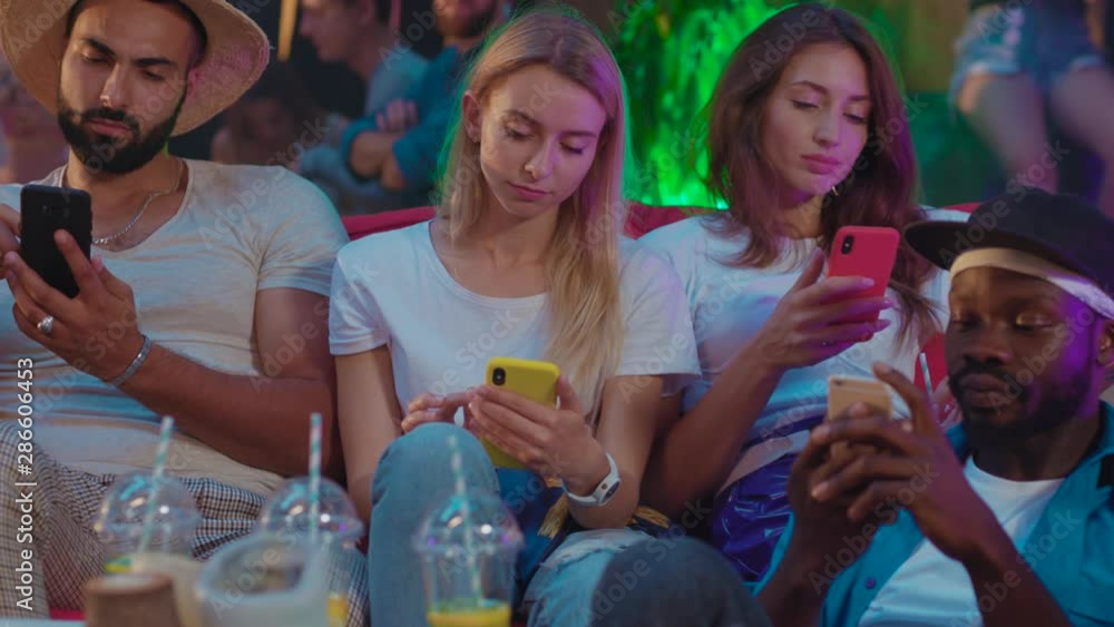 Group of friends using smartphones chatting online instead of live communication. Modern youth partying together in the club. Party time. Group of friends using smartphones chatting online instead of live communication. Modern youth partying together in the club. Party time.
