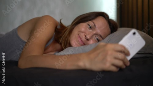 A lonely sick girl looks at her cell phone, counting the minutes until the pain subsides. A woman lies on the bed and hurts. There are antibiotics on the bedside tables. Virus Allergy Infection photo