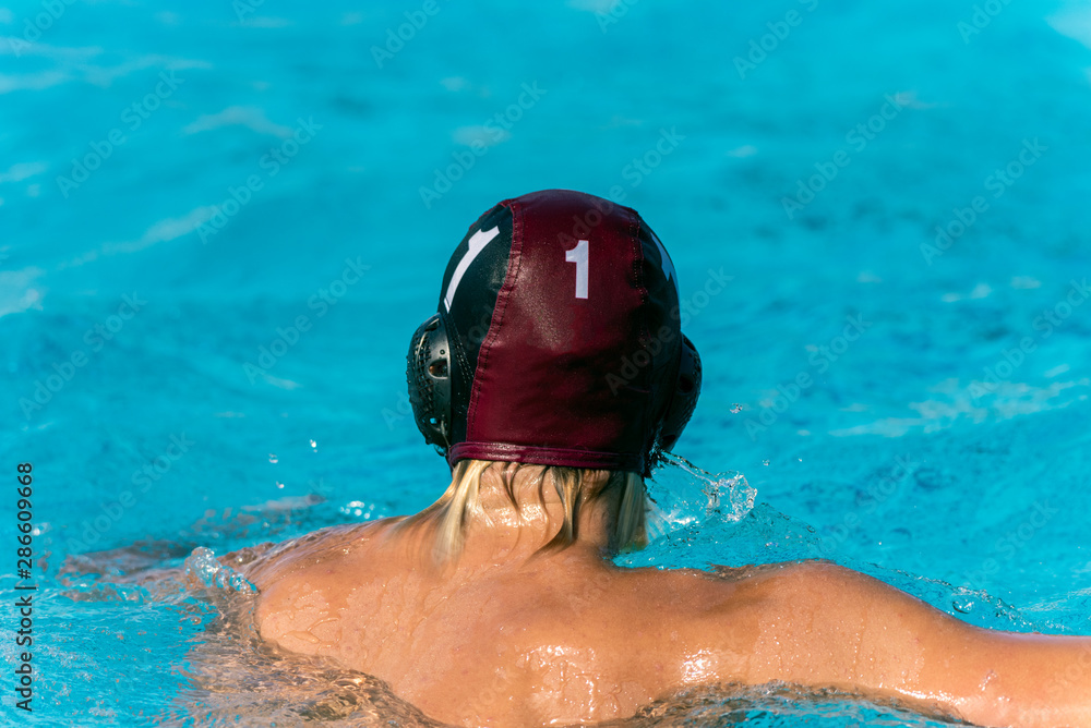 Water polo goalie number 1 treads water in swimming pool while wearing black uniform.
