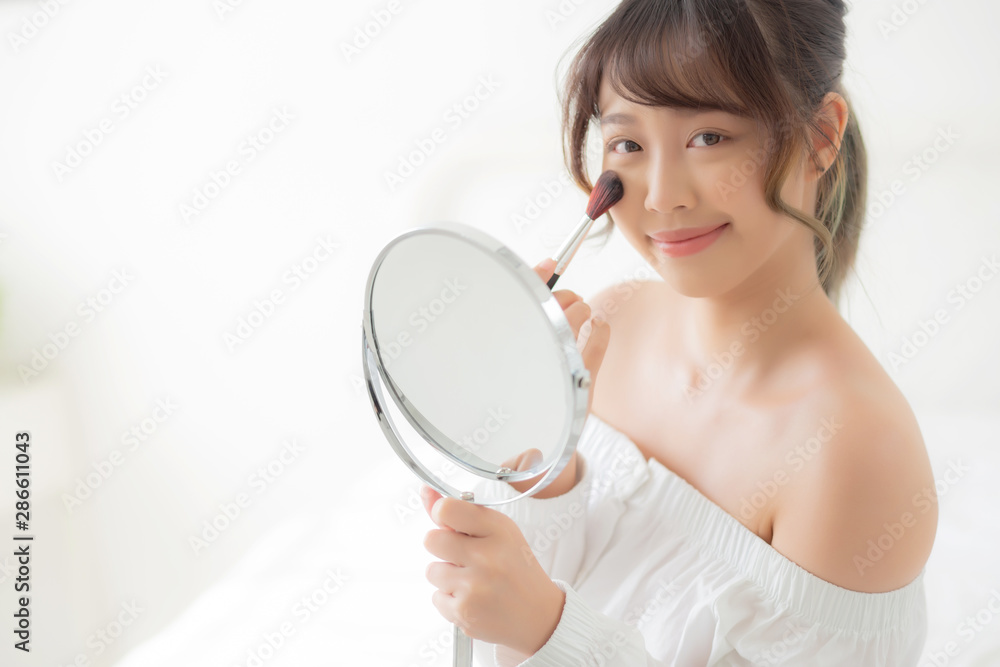 Beauty portrait young asian woman smile with face looking mirror applying makeup with brush cheek in the bedroom, beautiful of girl holding blusher, skin care and cosmetic concept. Beauty portrait young asian woman smile with face looking mirror applying makeup with brush cheek in the bedroom, beautiful of girl holding blusher, skin care and cosmetic concept.