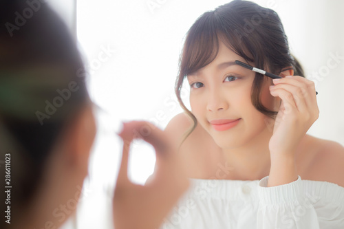 Beautiful young asian woman applying makeup eyebrows brush, beauty asia girl using cosmetic for make up style looking mirror at home, fashion female tweezing with natural, lifestyle concept.