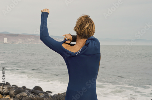 Fotografie Young male putting on his wetsuit ready for a surf session.