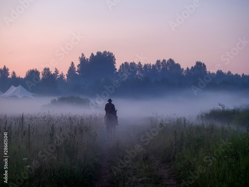 Silhouette of a man on a horse who rides through the morning fog © alexkazachok