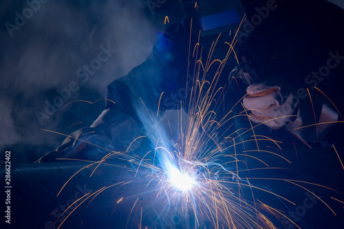 Professional welder and mask welding metal pipe on the industrial table.