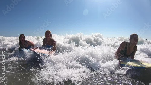 3 Young women riding a wave on boogie boards in the ocean as they have fun and laugh.