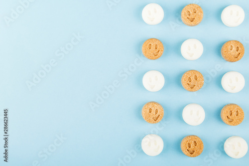 White and brown sugar smiles on blue background. Top view  copy space. Food background