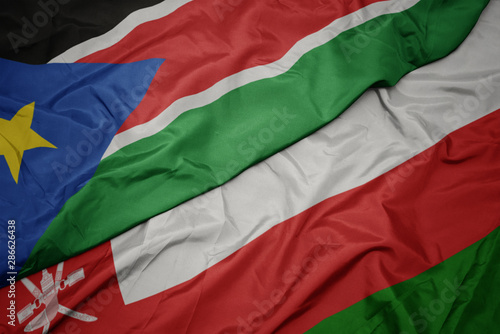 waving colorful flag of oman and national flag of south sudan.