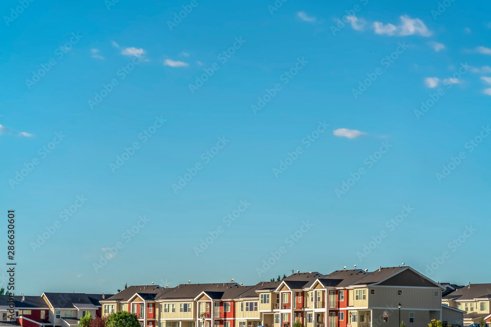 Fototapeta Blue sky on a sunny day over townhomes with white and red exterior wall