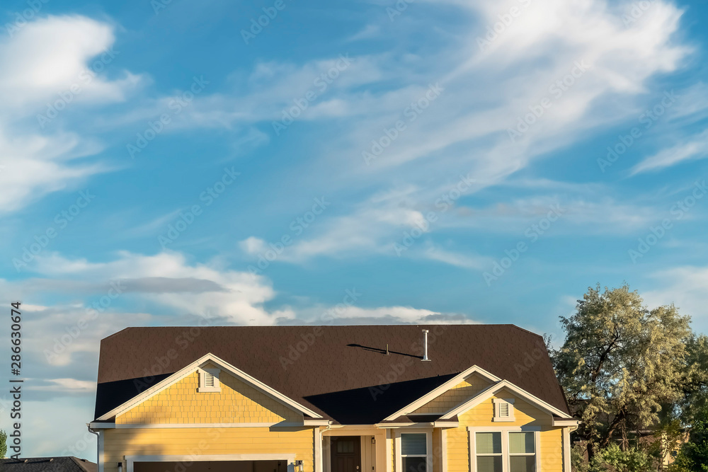 Home exterior with dark roof and cream wall viewed against sunny cloudy blue sky Home exterior with dark roof and cream wall viewed against sunny cloudy blue sky