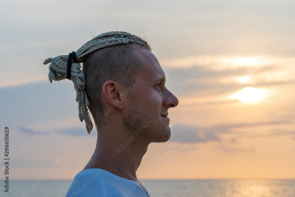 Silhouette of a young guy with dreadlocks on his head near sea during sunset. Close up portrait