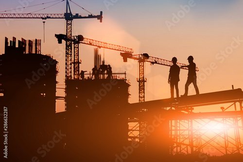 Tablou canvas Silhouette Two engineers consult and inspect high-rise construction work over blurred industry background with Light fair