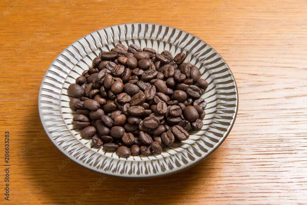 Fototapeta premium Coffee beans on a plate placed on a wooden table.