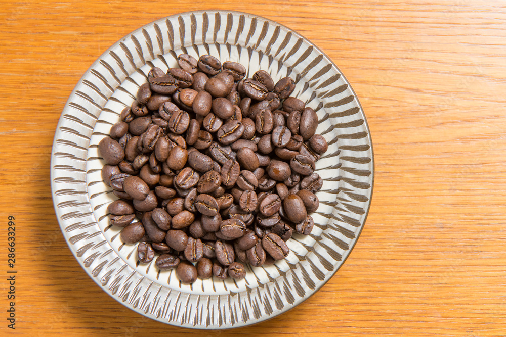 Fototapeta premium Coffee beans on a plate placed on a wooden table.