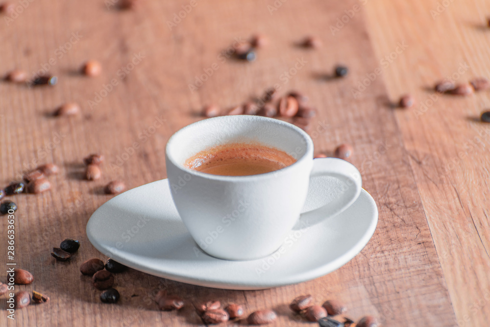 Aerial view of a white porcelain cup with espresso and roasted coffee beans on a wooden table. Relaxation concept and coffee aroma.
