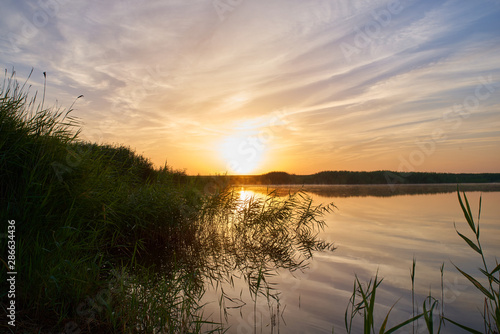 Spectacular morning landscape of bushy river banks and smooth river waters against warm colors of early morning sun. Magnificent sunrise over distant forests and the river in Russian countryside. 